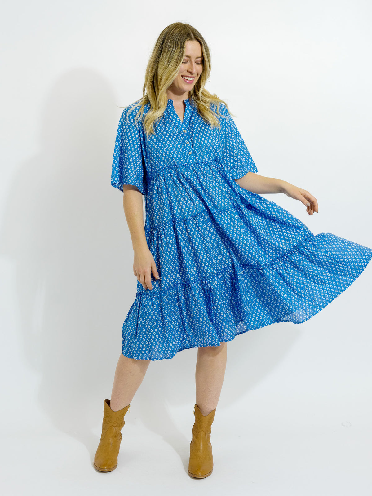 A model wearing a knee-length blue and white dotted dress with a V-neck and half sleeves, paired with brown boots.